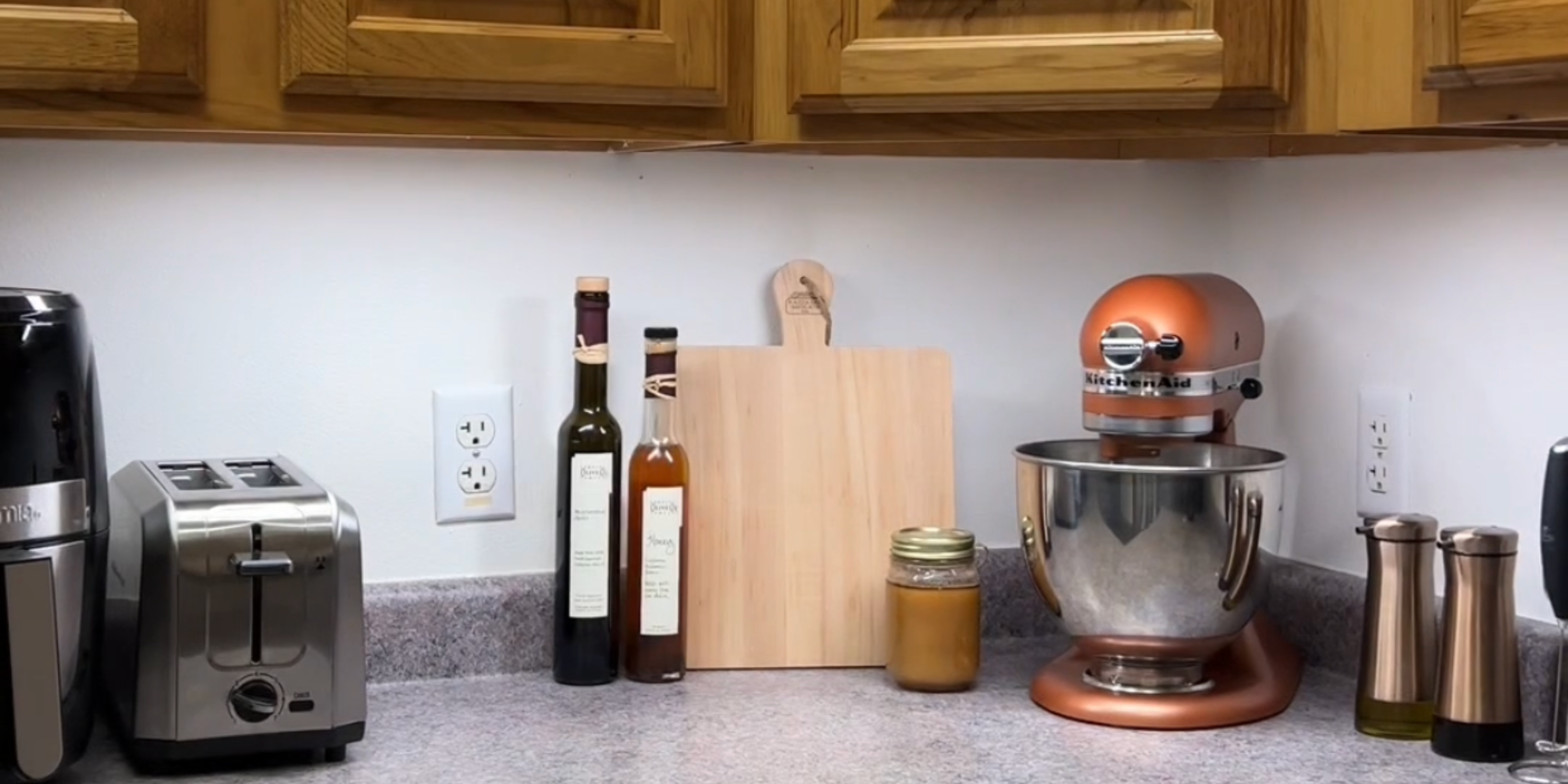 A well-organized kitchen countertop featuring a stand mixer, toaster, oil and vinegar bottles, cutting board, and a jar.
