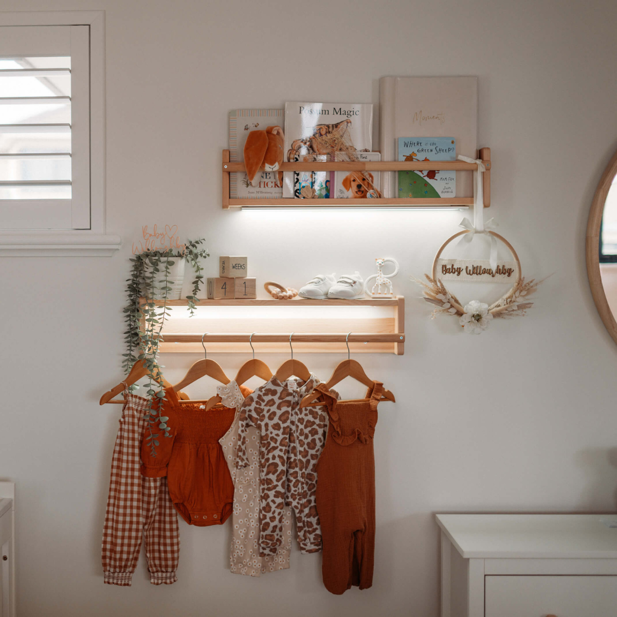 Cozy nursery display featuring hanging baby clothes, books, a growth chart, and a decorative wreath with "Baby William Abby."