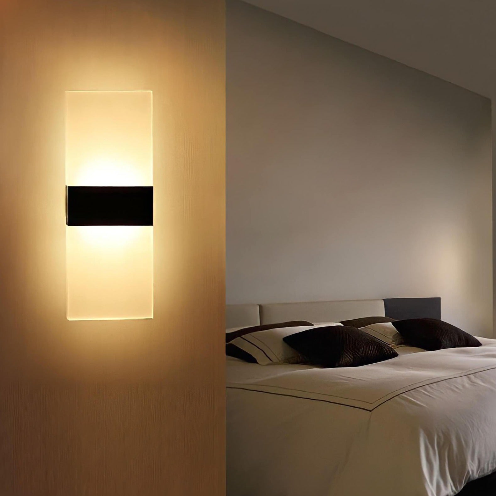 Modern wall sconce illuminates a bedroom with soft light, featuring a sleek design next to a neatly made bed with dark pillows.